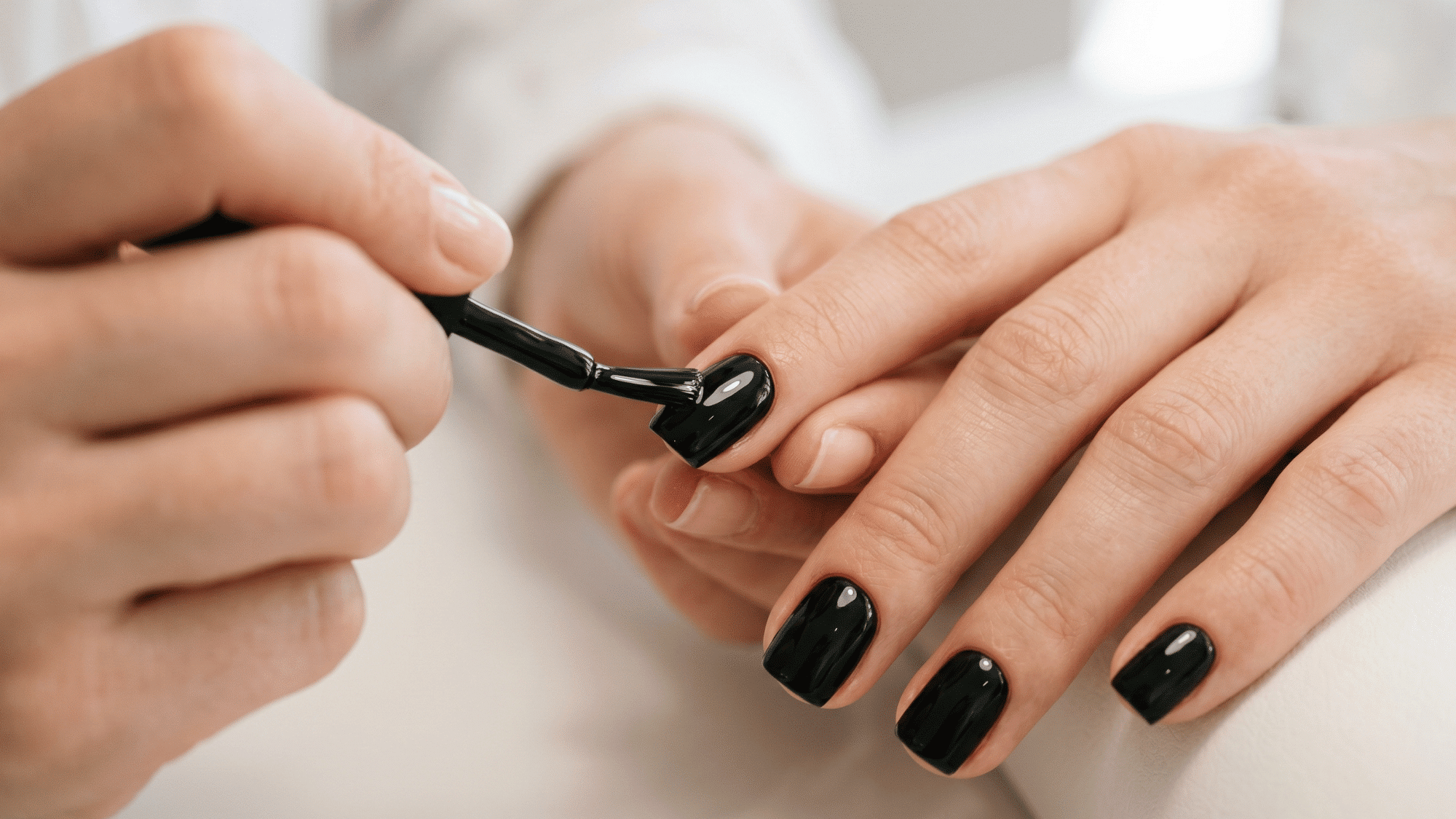 a hand applying smooth black gel nail polish on nails