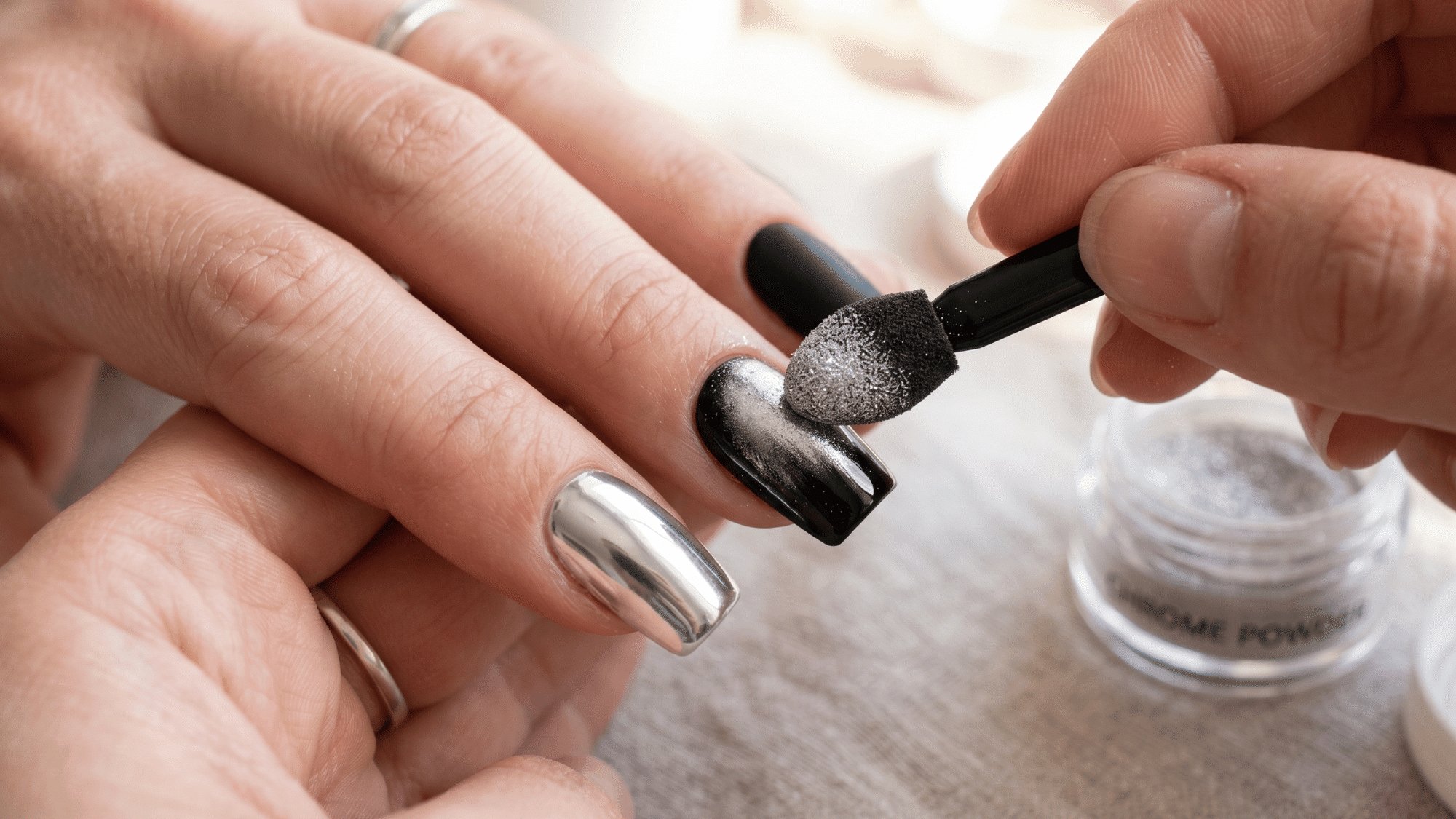 chrome powder being rubbed onto nails using a sponge applicator