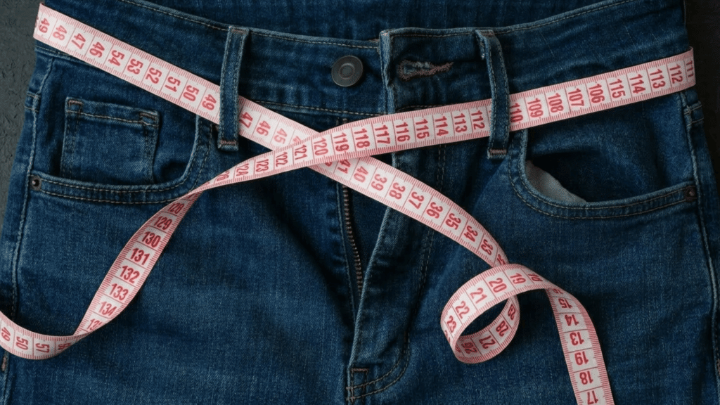 close up of jeans with measuring tape wrapped around waist showing clothing measurement and sizing concept