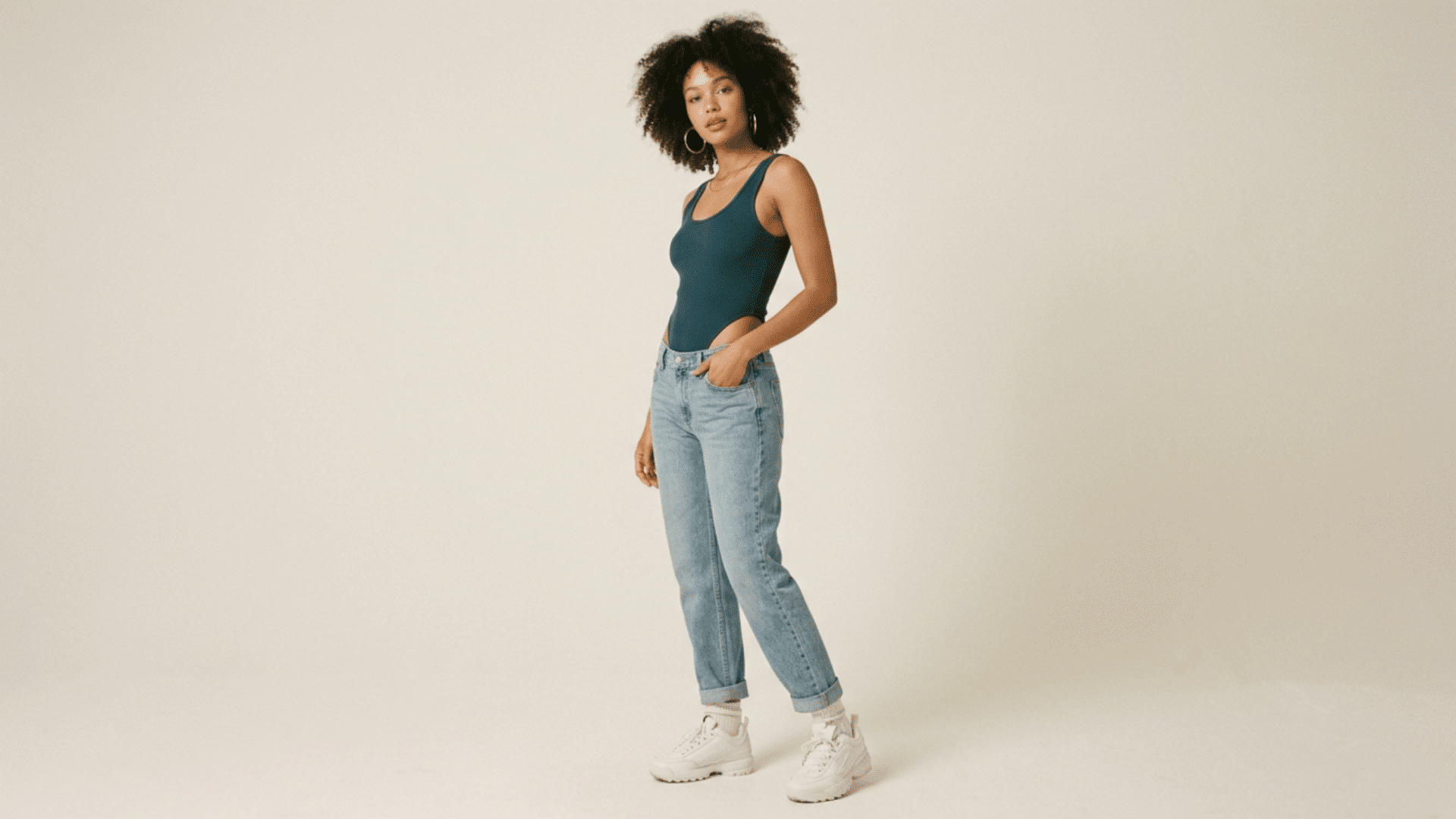 woman posing in high-cut one-pieces with jeans outfit with sneakers in studio setting with neutral background and soft lighting