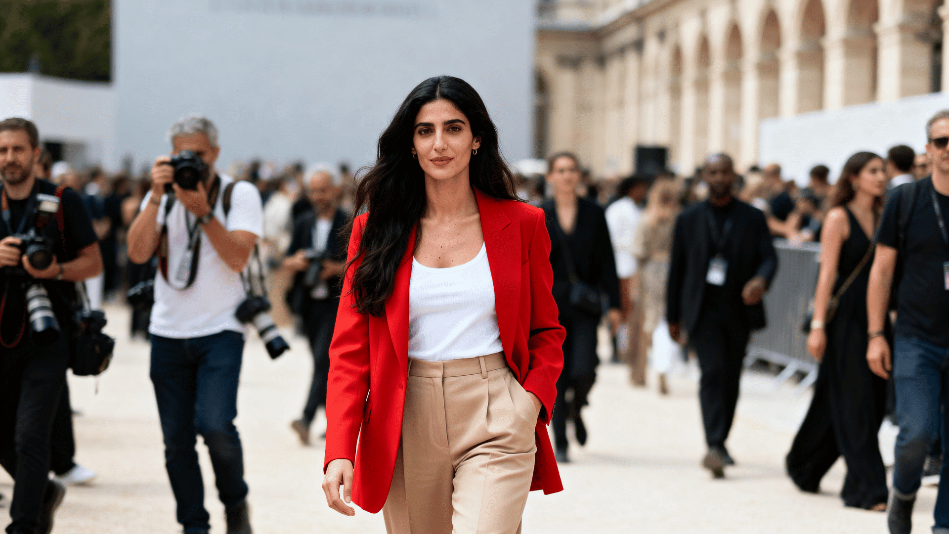 woman wearing a bright red blazer with a white tank top and beige tailored trousers at a fashion week venue.