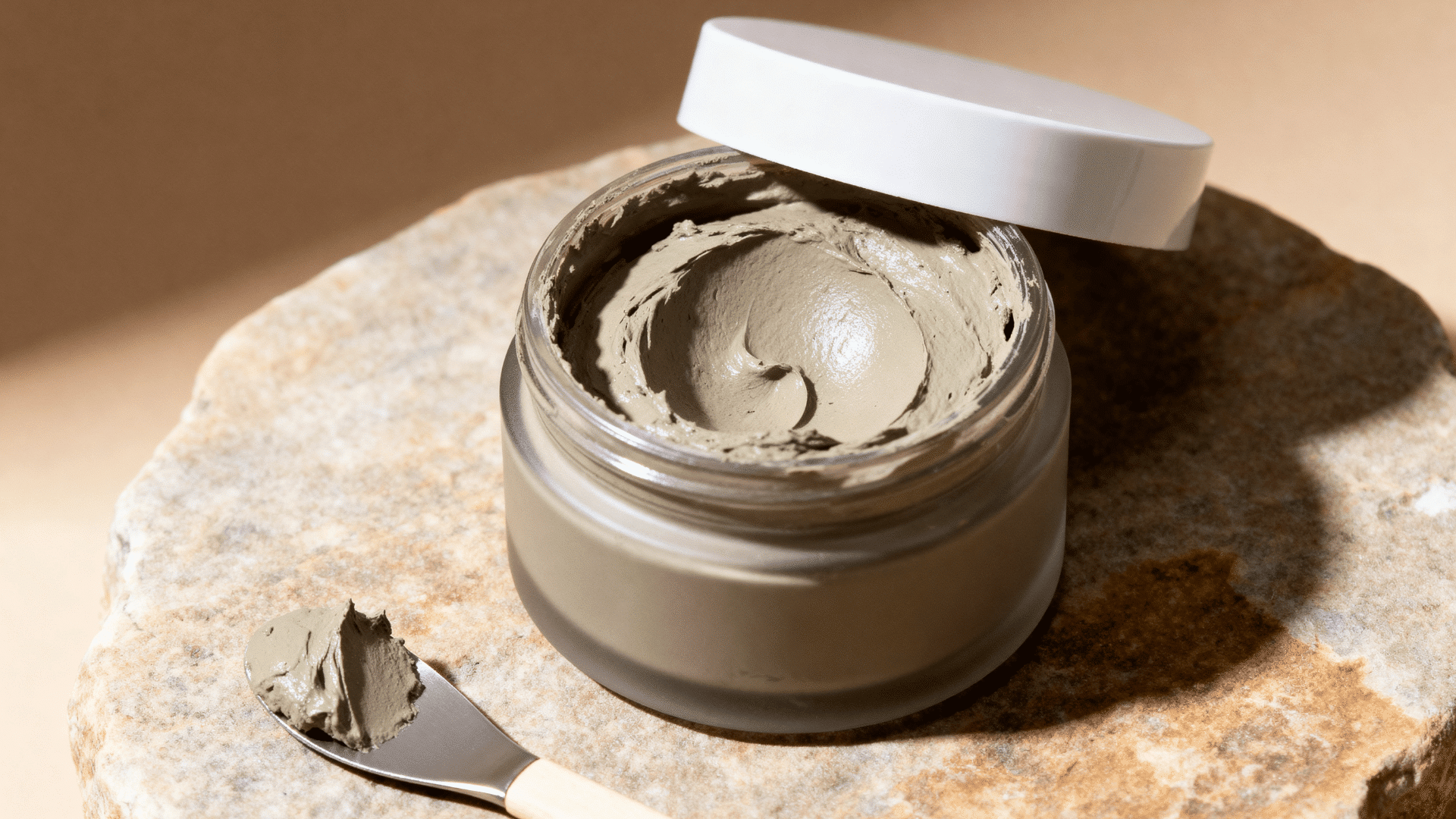 open clay mask jar with a skincare spatula on a wooden surface in an earthy spa-inspired setting.