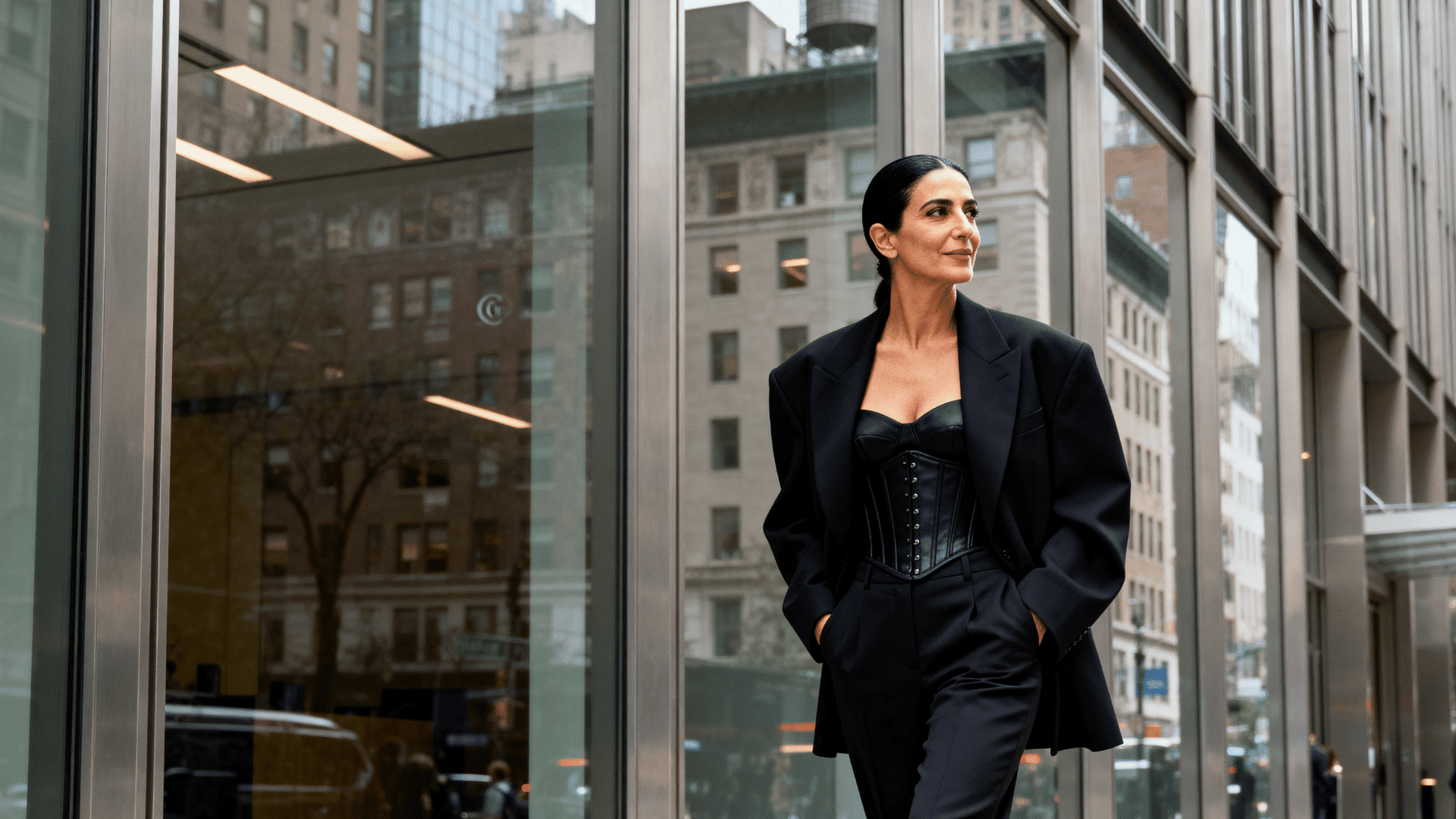 woman wearing a corset under a tailored blazer with matching trousers in a modern business district with city buildings behind her.
