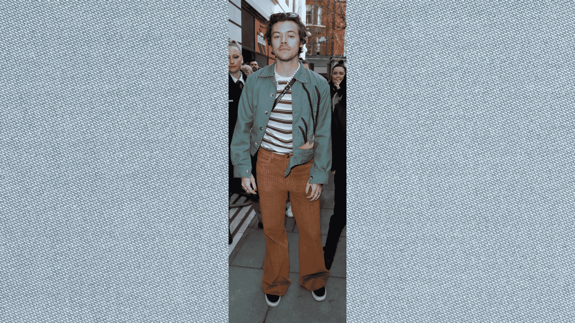 man standing on a city street wearing green embroidered jacket over striped shirt and brown corduroy flared pants with sunglasses
