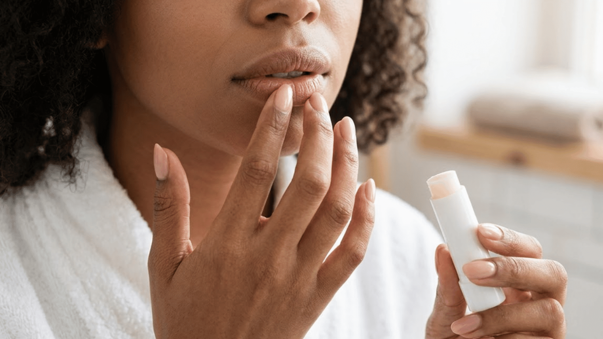 woman applying lip balm to dry lips while holding a white balm tube during her daily lip care routine