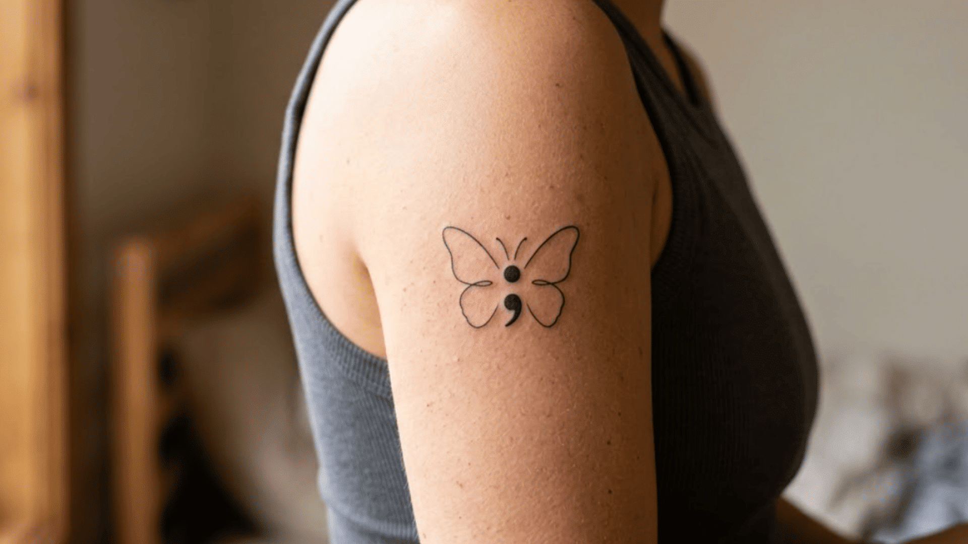 butterfly semicolon tattoo on upper arm, with fine black lines and a simple mental health awareness design