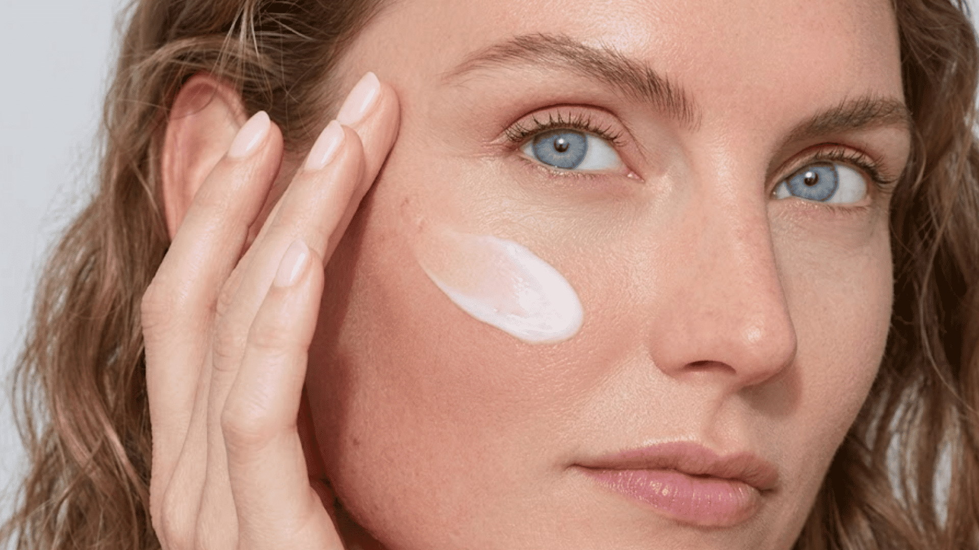 woman applying moisturizer to her cheek as part of a gentle skincare routine during the skin purging stage