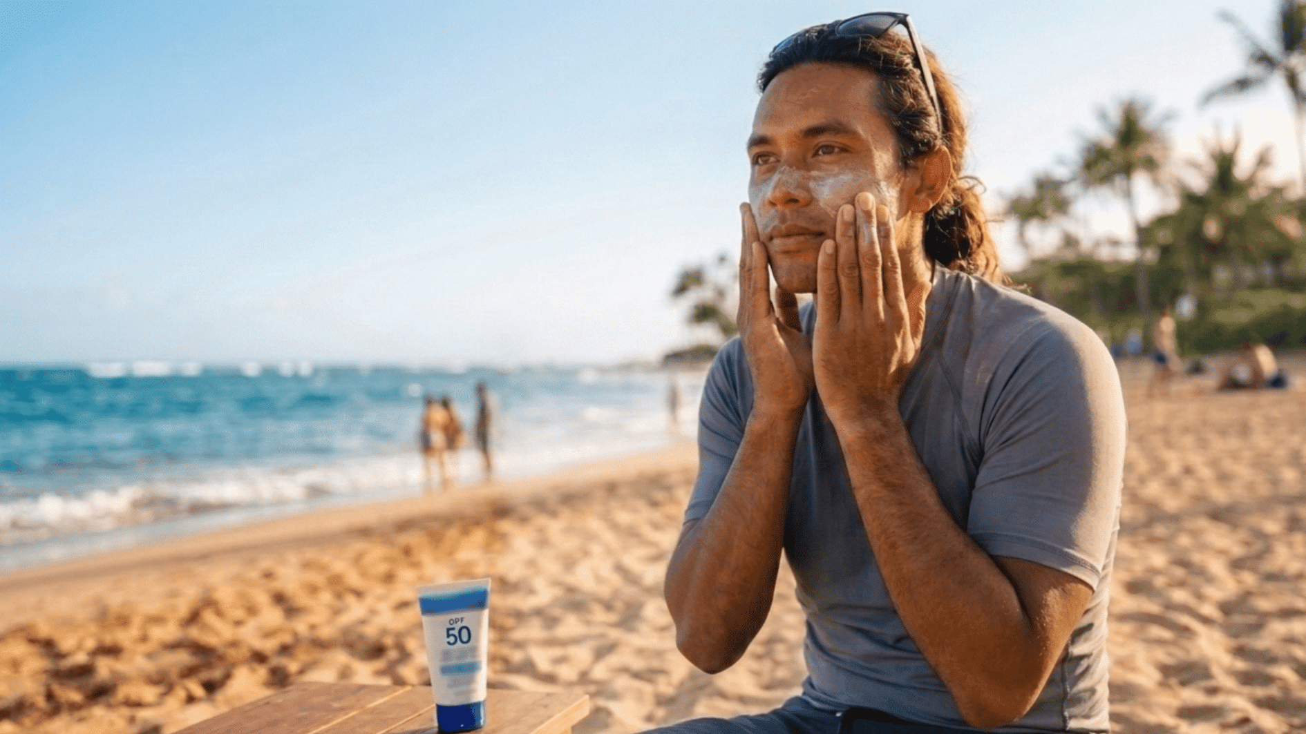 man applying sunscreen to his face while sitting at a beach