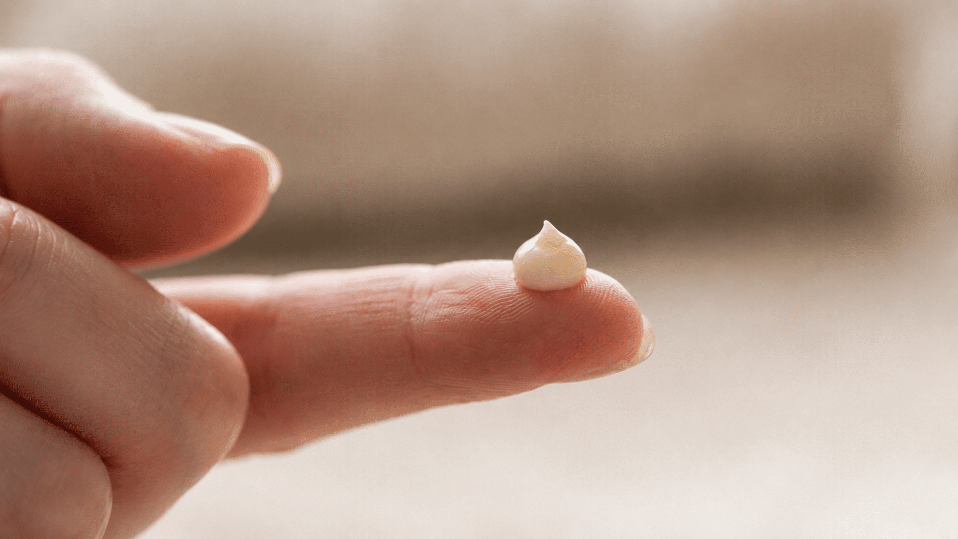 pea-sized amount of retinol eye cream on a fingertip beside an open skincare tube