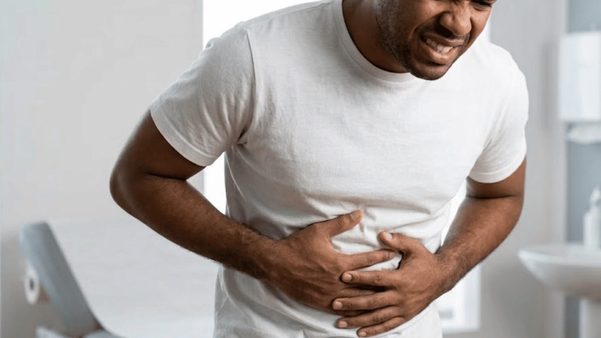 man clutching his stomach in pain while standing in a bathroom, showing signs of digestive discomfort