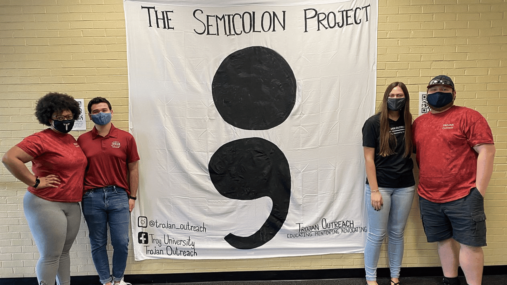four people pose beside a large Project Semicolon banner during an indoor mental health awareness event