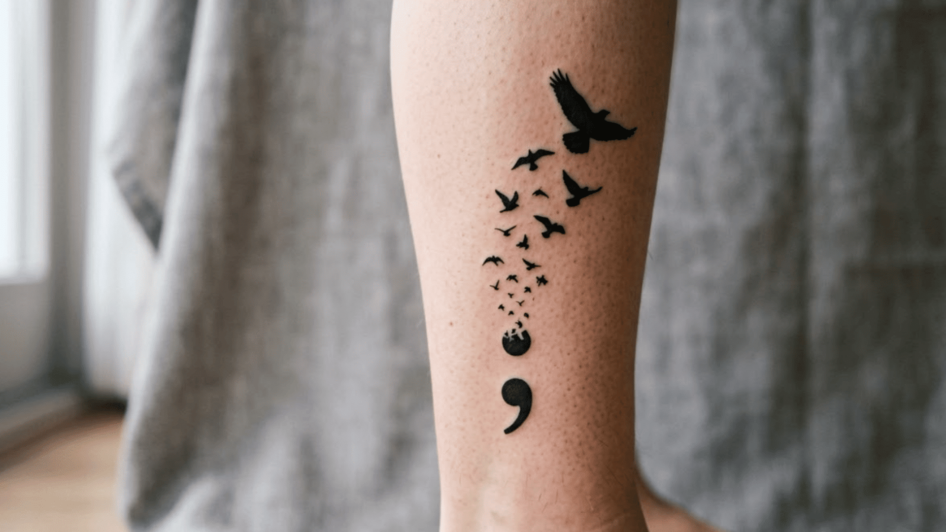 black semicolon tattoo on ankle with a flock of birds rising upward, symbolizing hope and moving forward