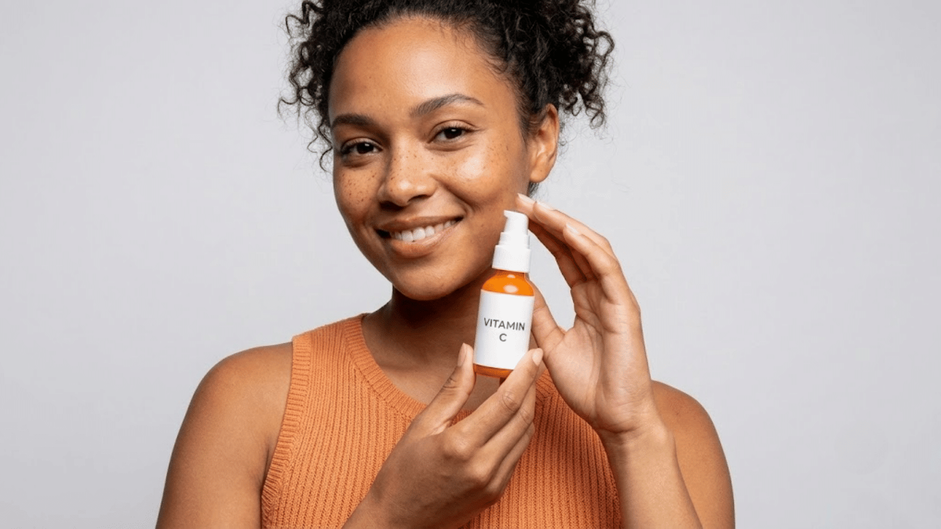 woman holding vitamin c serum bottle for skincare routine and showing a healthy glowing complexion