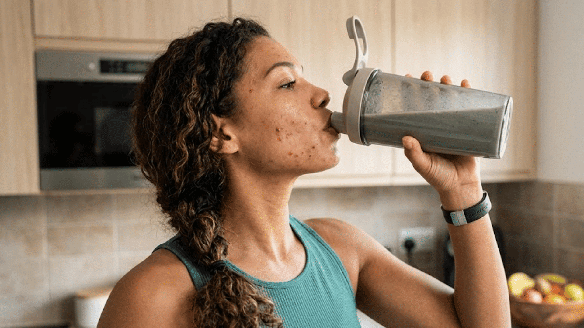 woman with facial acne drinking a protein shake from a shaker bottle in a bright kitchen after exercise