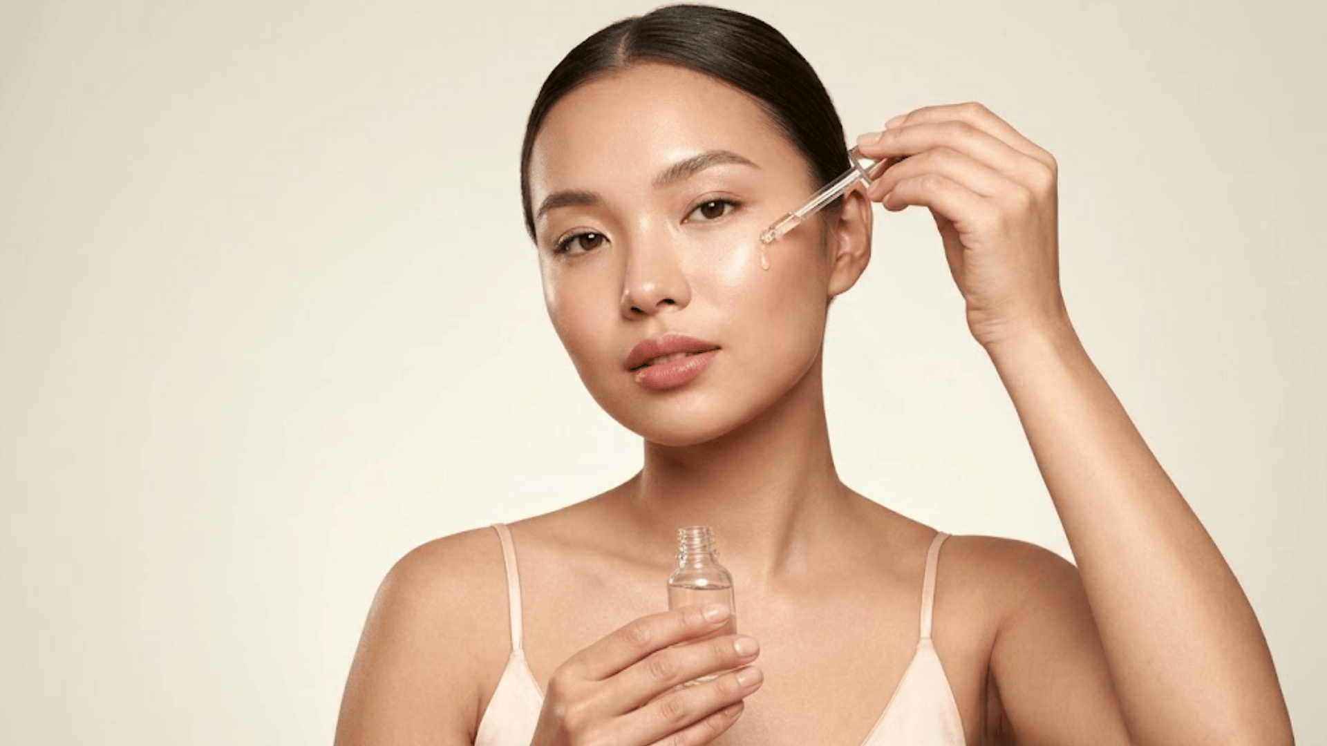 woman applying facial serum with a dropper while holding the skincare bottle