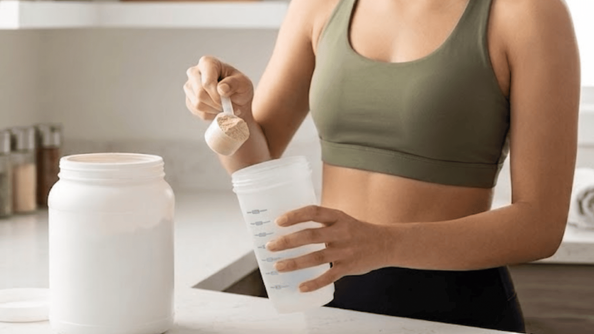 woman preparing a scoop of creatine powder in a shaker bottle at a kitchen counter